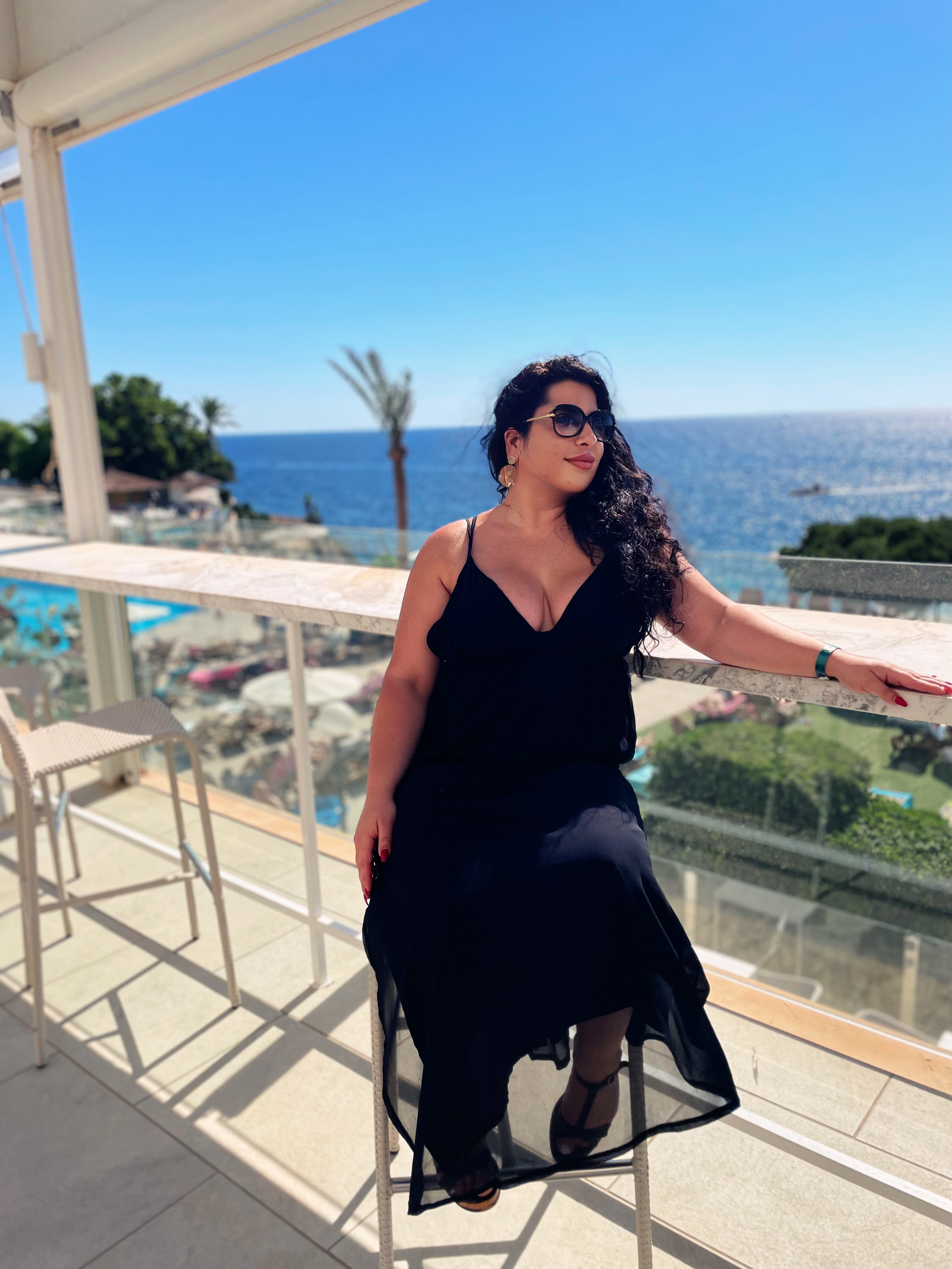 reiche geldherrin sitzt im kleid an strandbar und geniesst luxusurlaub durch geldsklave